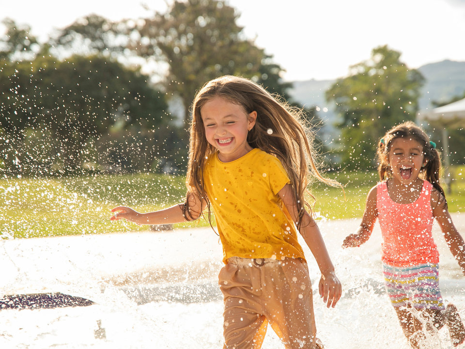 Photograph of two girls running through park fountains.