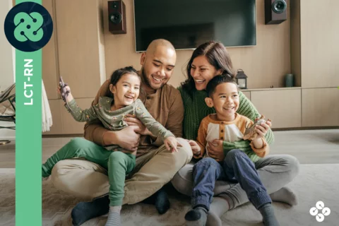 Photograph of a family of four sitting on the ground in front of their television.