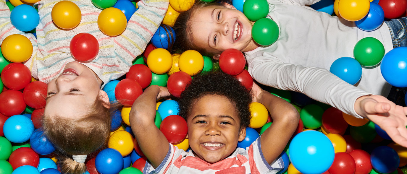 Photograph of three children laying in a multi-colored ballpit.