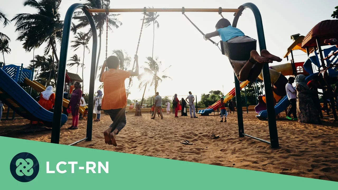 Photograph of two kids swinging on swings with their backs to the camera in the foreground. 