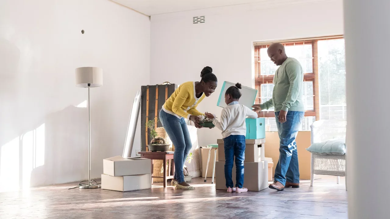 Photograph of a family of three moving into a new home. Boxes scattered and sun shining in the window.