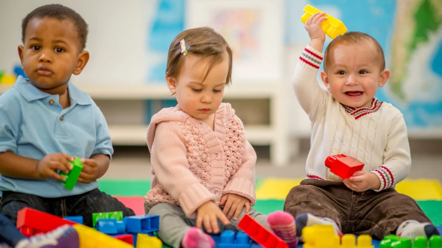 Three children playing with large lego blocks in a preschool