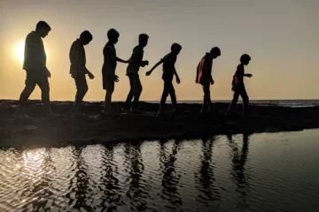 Group of kids walking along the beach at sunset.