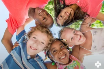 Photograph of five children huddled around a camera.