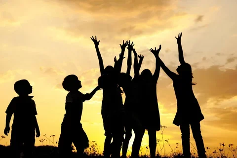 Photograph of a group of children playing, silohuetted by the sunset.