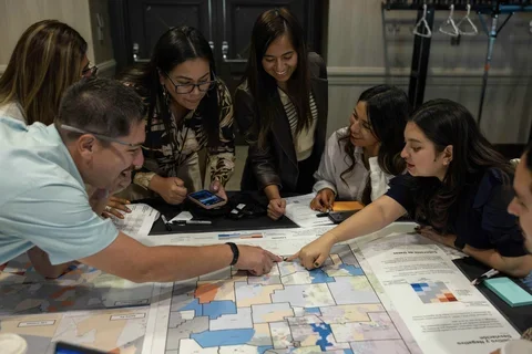 Photograph of a group of people examining a poster on a table while talking.