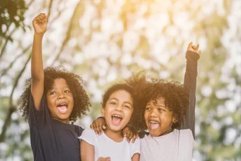 Photograph of three children smiling and cheering towards the camera