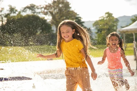 Two girls running through park fountains.