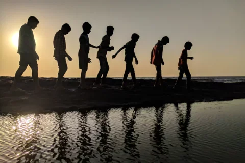 Group of kids walking along the beach at sunset.