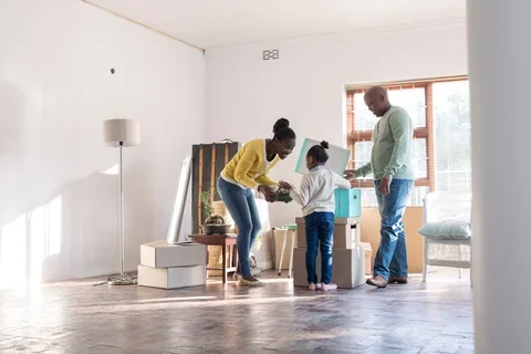 Photograph of a family of three moving into a new home. Boxes scattered and sun shining in the window.