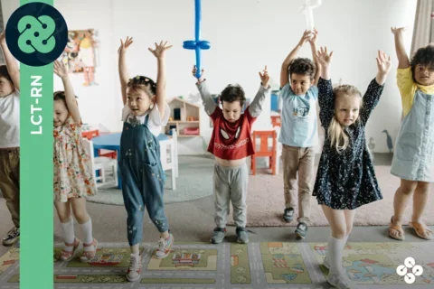 Photograph of 7 children dancing while in a preschool play area.