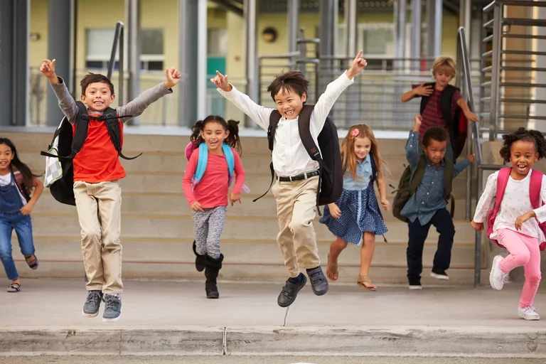 Children running towards the camera in front of a school.