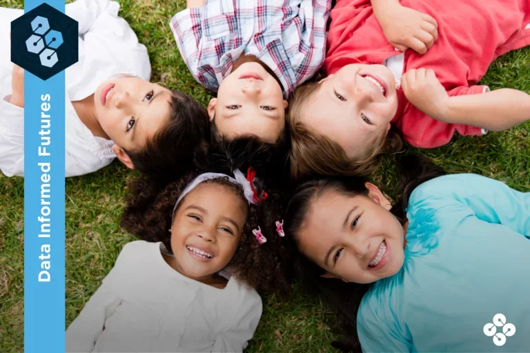 Five children laying on the grass smiling at the camera.