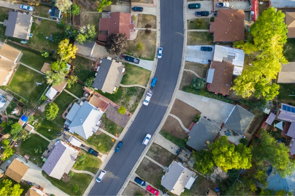 Sky view of neighborhood with streets, houses, and cars in street.