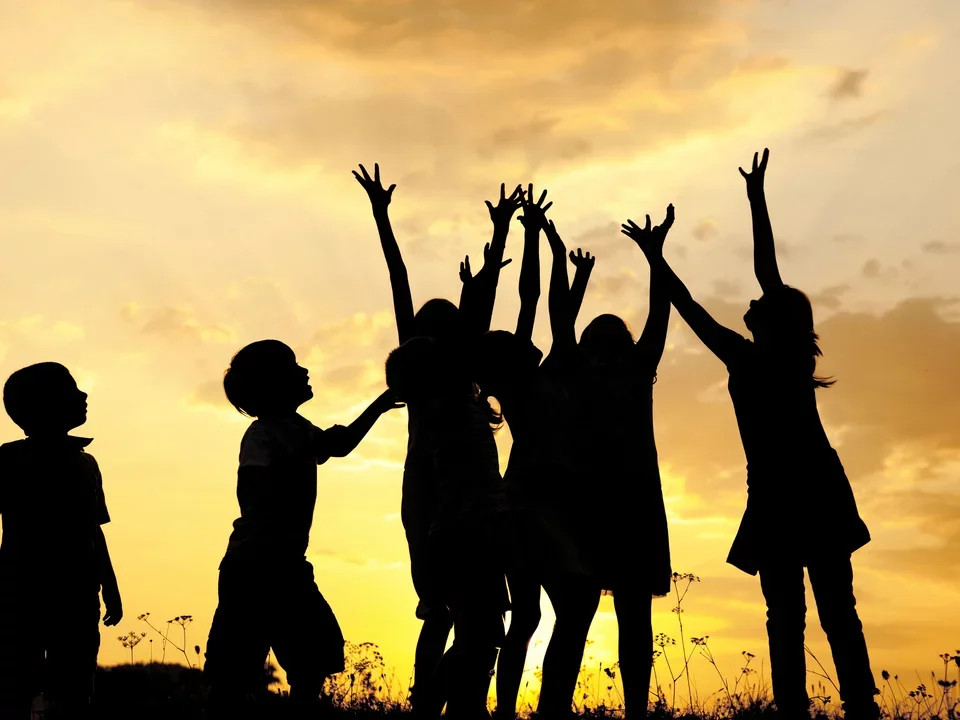 Photograph of a group of children playing, silohuetted by the sunset.