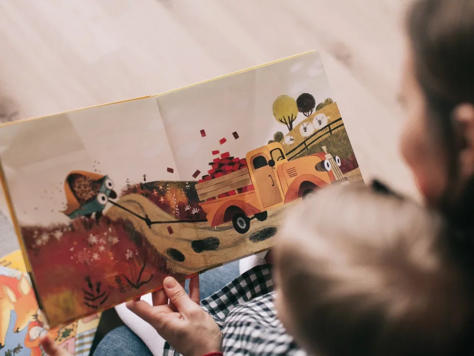 Photograph of mother holding her child in the foreground with a children's picture book in focus in the background. 