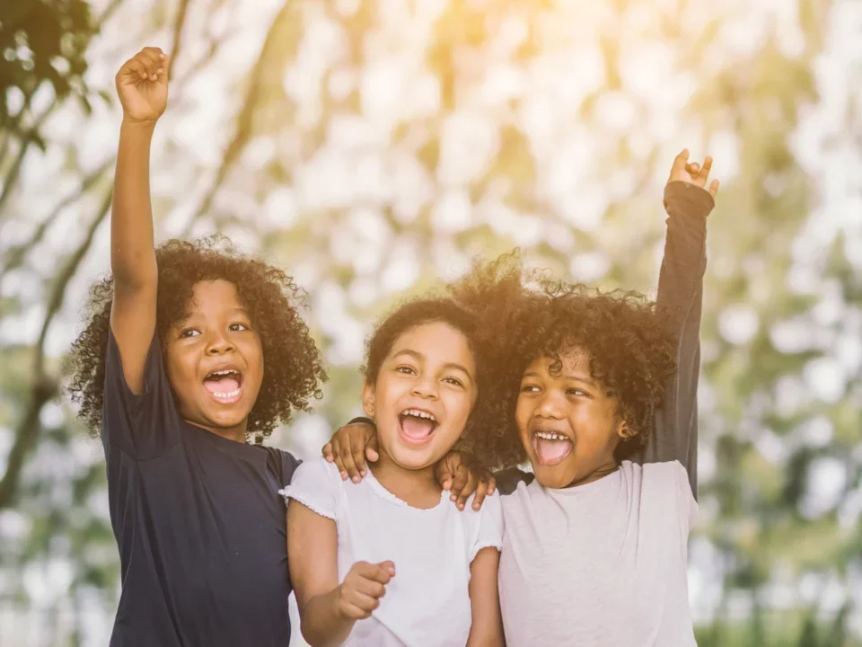 Photograph of three children smiling and cheering towards the camera
