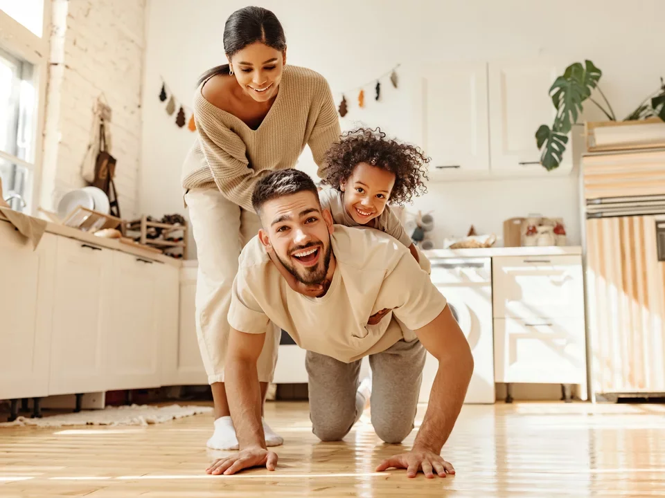 Photograph of a family of three playing together in the kitchen of the home.