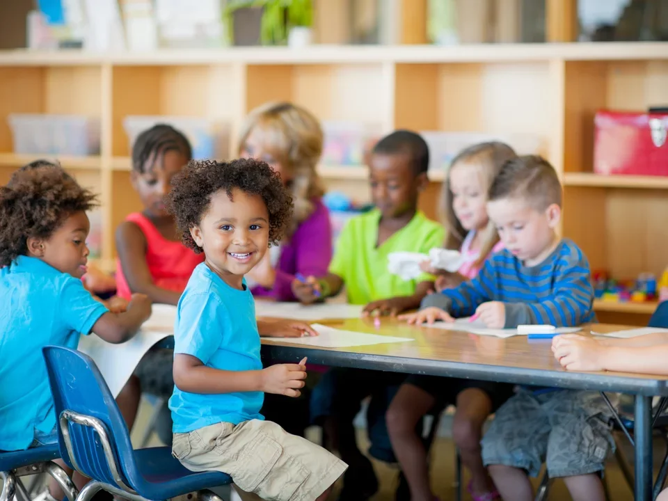Group of children smiling at the camera while sitting in a classroom.