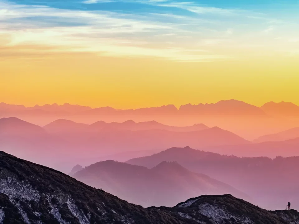 Photograph of a mountain range at dusk, with a purple, blue, and yellow and pink sky.