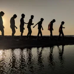 Group of kids walking along the beach at sunset.