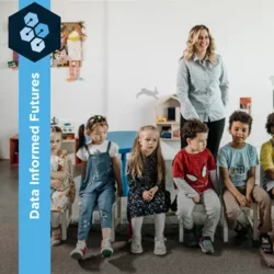 Photograph of kindergarten students sitting in class with two teachers in the foreground.