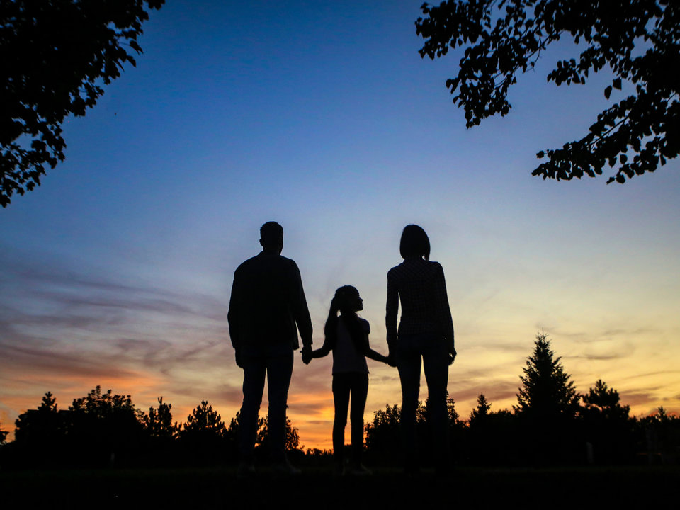 Photograph of a family standing amongst the trees silhouetted against the sunset.